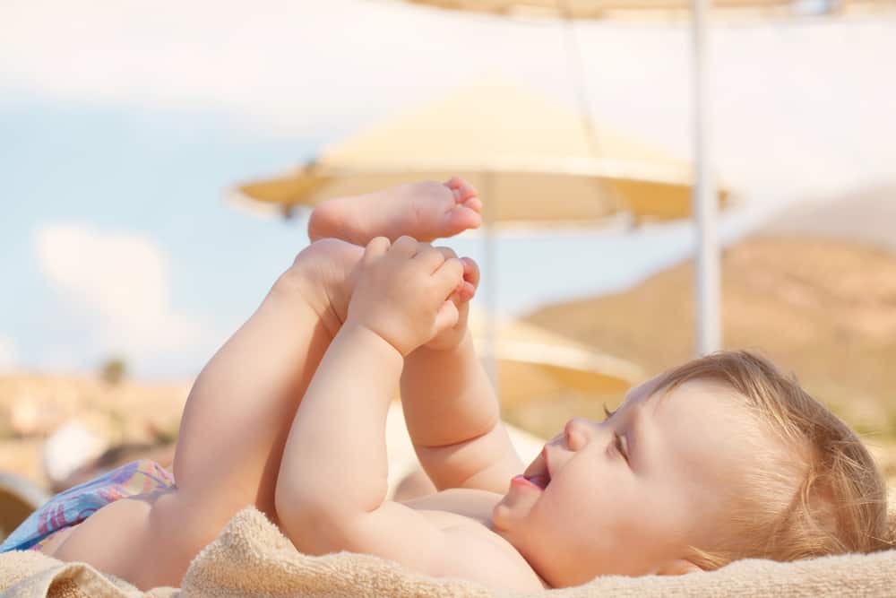 Happy baby on beach lying on lounger