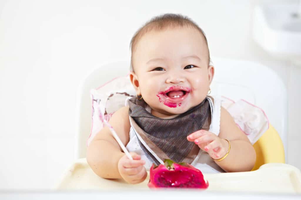 baby girl smiling eating red fruit