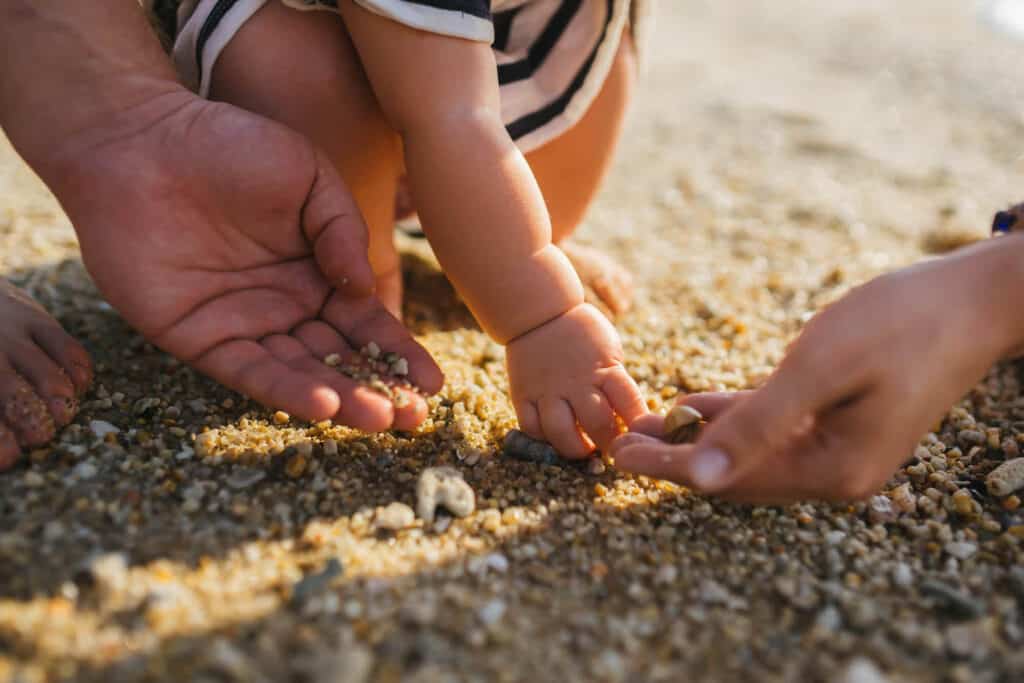 baby girl with parents touching sand earth