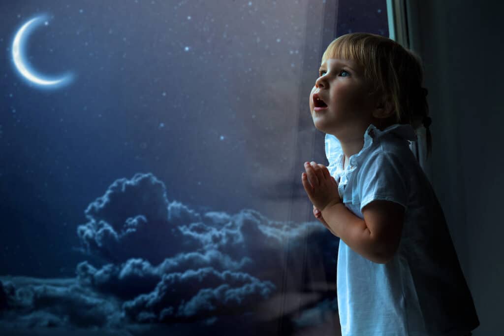 little girl looking out window at moon night sky