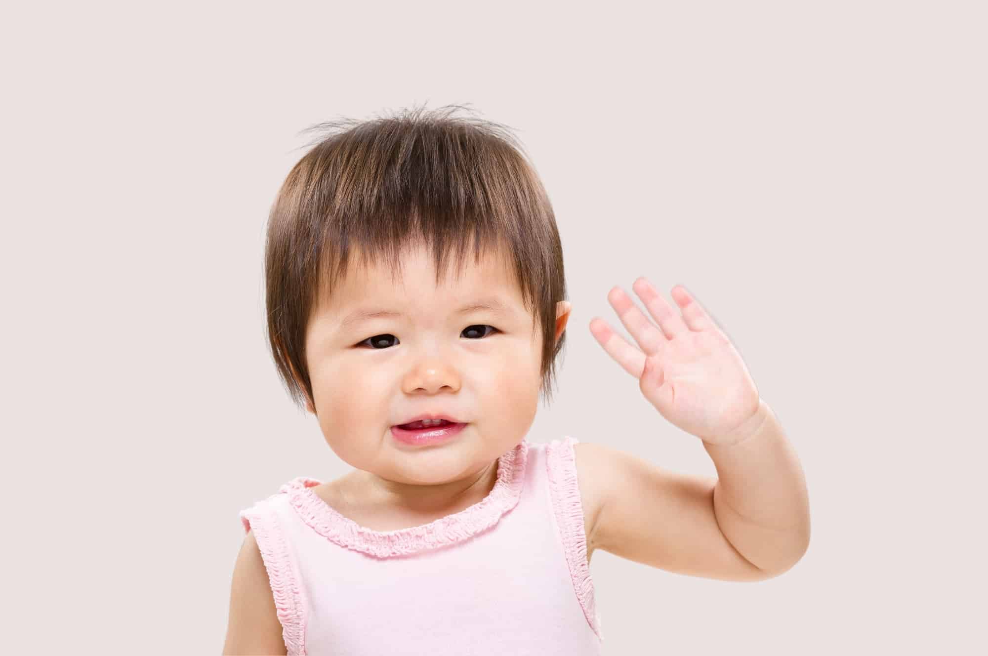 baby girl waving pink shirt beige background