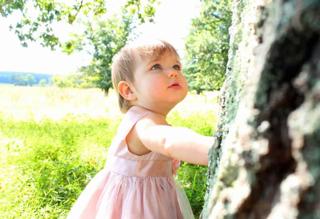baby girl touching tree looking up