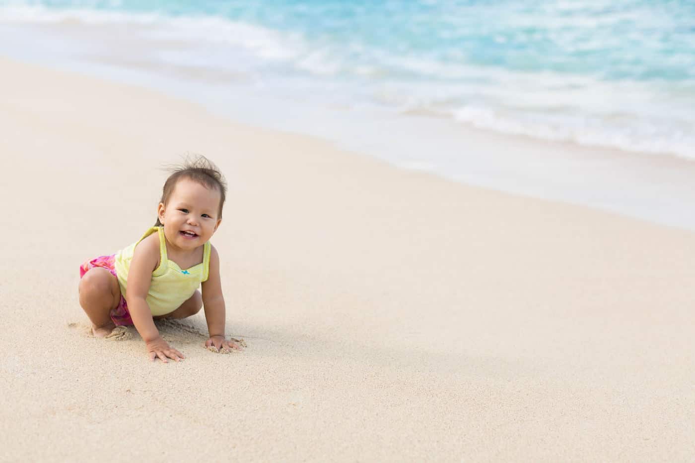 baby girl sitting on beach next to ocean