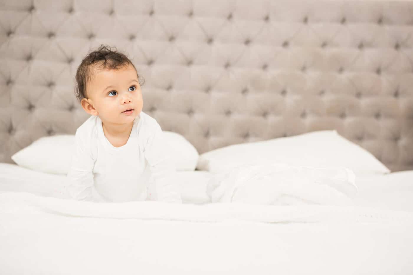 baby boy in white sitting on bed