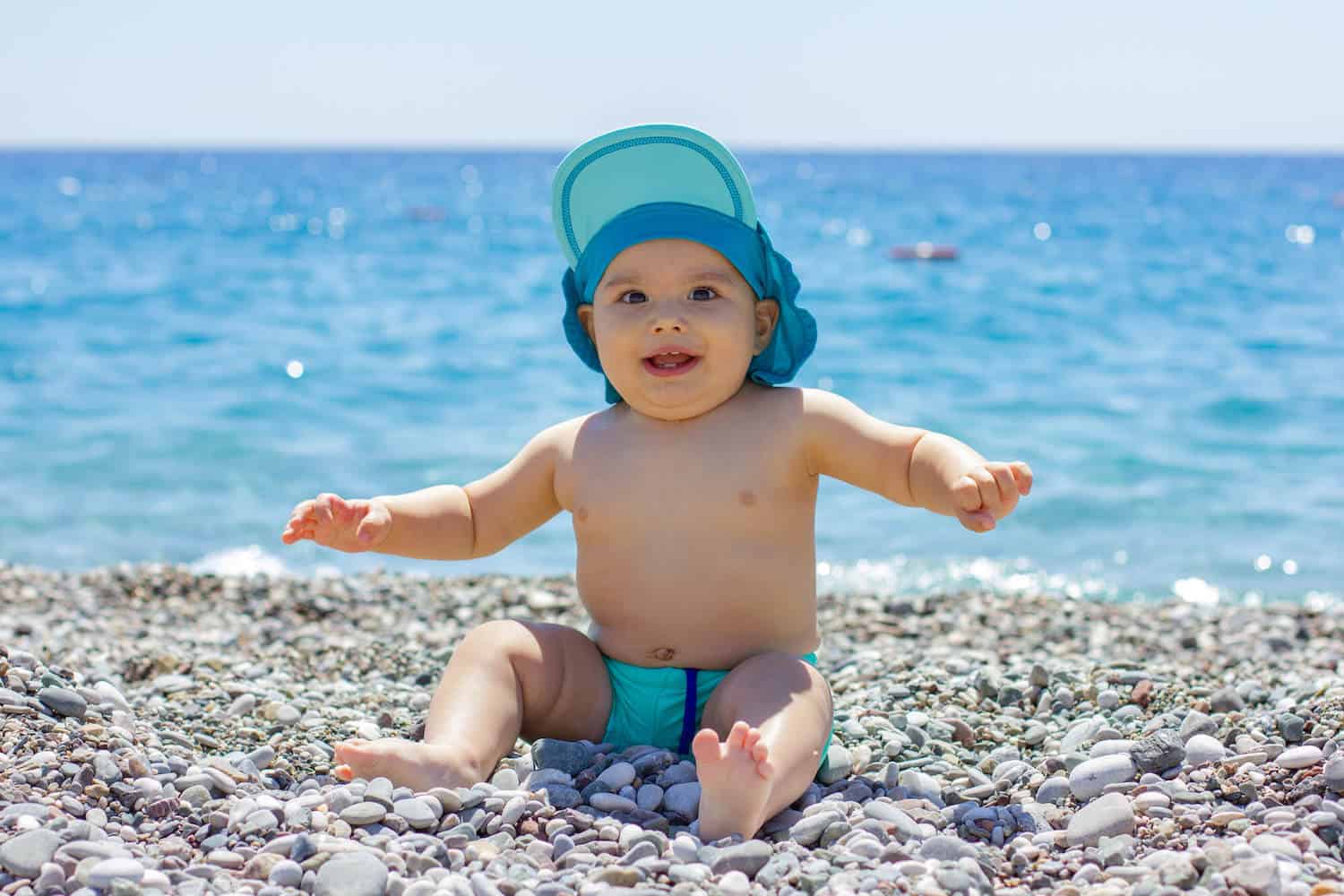 baby boy sitting on beach in front of water