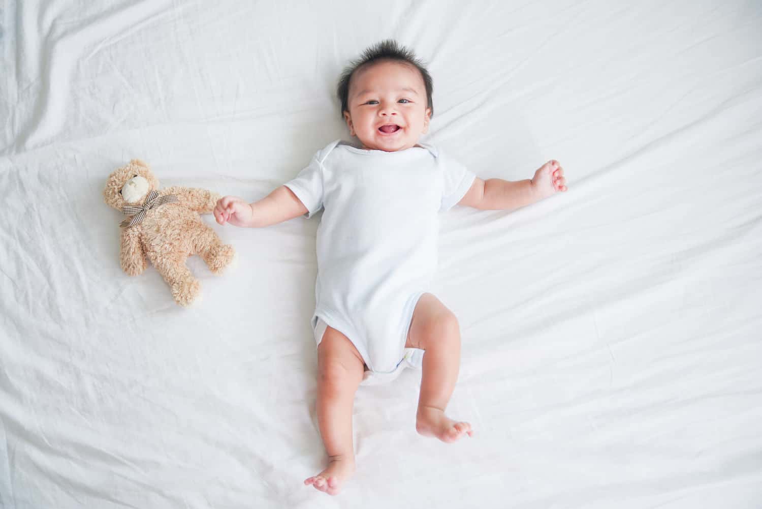 smiling baby boy with teddy bear on bed